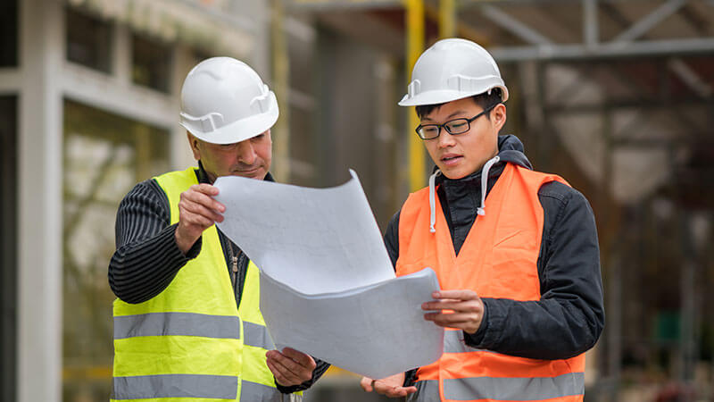 Two contractors reviewing building plans at a construction site.