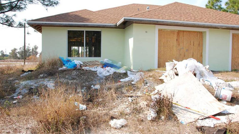 A house with missing and boarded windows, and litter in the front yard.