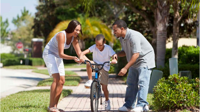 Image of parents teaching their son to ride bike.