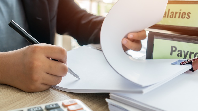 image of a peson with a legal pad and calculator.  Two binders int he background labeled salaries and payroll. 
