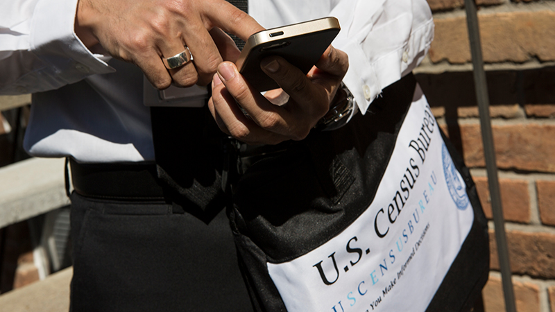 Man using phone, carrying US Census bag.