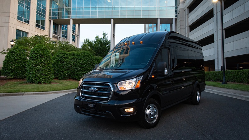 Black van parked in front of a modern building complex with glass walkway and greenery.