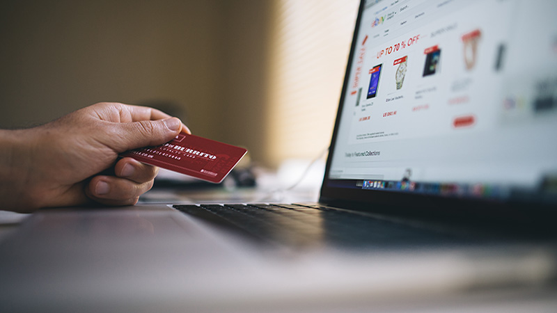 Hand holding a credit card in front of a laptop computer. Links to news item.