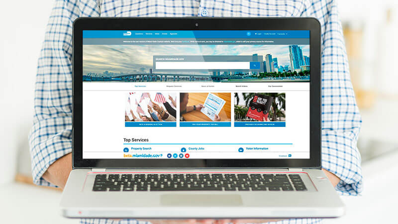 Man holding laptop displaying Miami-Dade County portal.