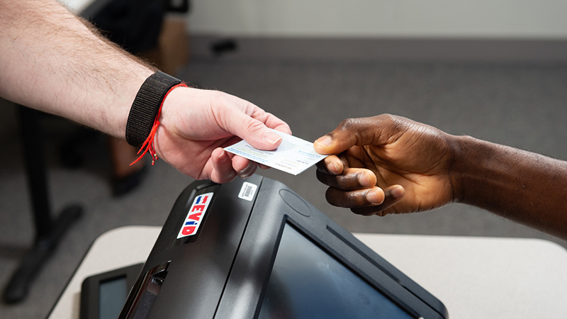 Close up photo of someone handing in their voter ID card to someone else