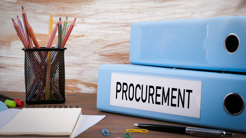 A desk with pencil cup holder, papers, binder labeled PROCUREMENT