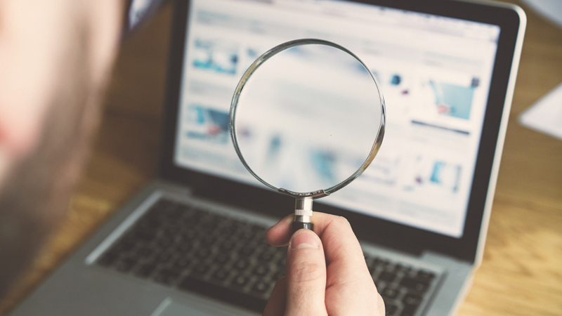 Man holding a magnifying glass up to a laptop screen