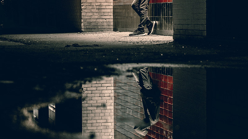 Image of person standing against the wall's reflection within a puddle