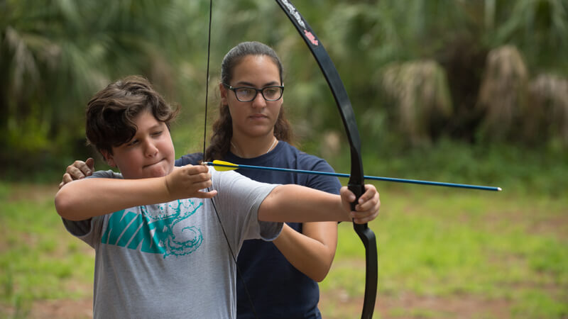 Boy being instructed on how to hold a bow and arrow for a practice shot.