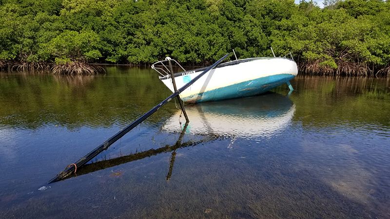 fiberglass sailboat, stripped of its rigging, hard aground in a seagrass meadow
