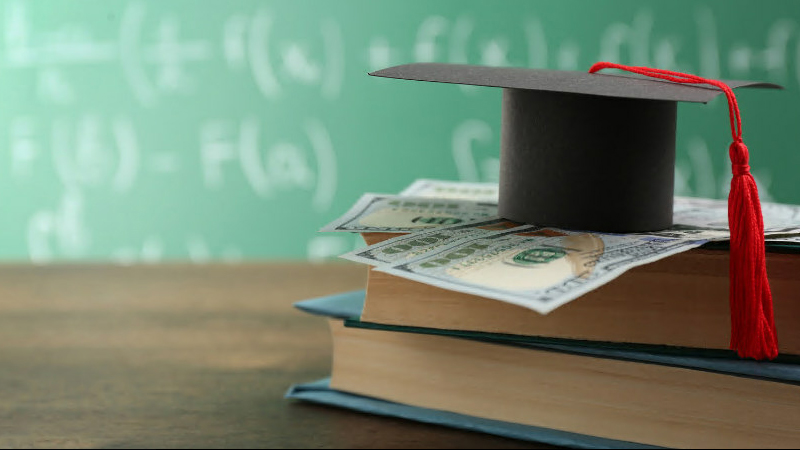 money and a graduation cap on top of two books on a table