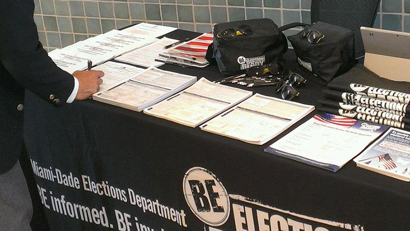 Table with forms laid out. There's a person on one side of the table filling out a voter registration form.