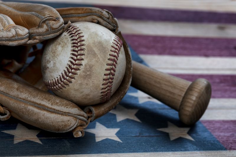 image of baseball bat, baseball and glove with american flag in background
